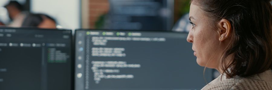 Aspiring female entrepreneur sitting in front of two computer monitors using ChatGPT generative AI to create a business plan.