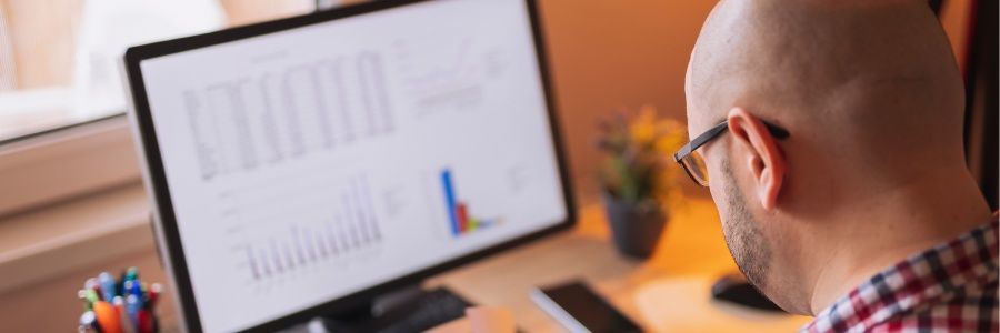 Male entrepreneur sitting in front of a computer monitor reviewing small business financial forecasts and exploring if ChatGPT can help him refine them.