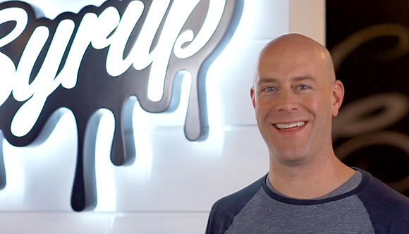 Jason Ogden posing in front of a Syrup Marketing sign